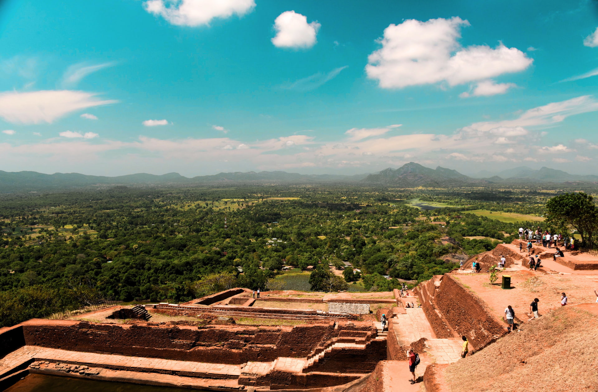 The ancient red brick ruins of a royal palace at the summit of Sigiriya rock fortress, looking out over the vast green canopy of Sri Lanka's dry zone